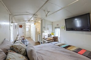 Quarto compacto com cama, escrivaninha e televisão.