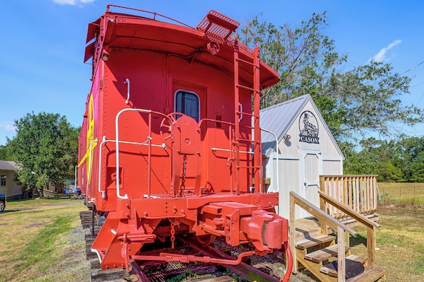 A red train caboose with a small wooden structure beside it.