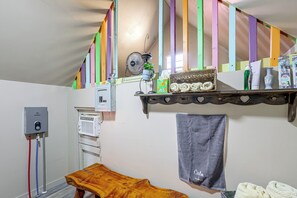 Ein Zimmer mit einer hölzernen Sitzbank, einem Handtuch an der Wand, einem Ablagefach mit Pflegeprodukten und einem Ventilator.