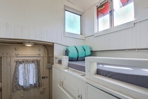 A compact, well-lit cabin with a door, a small window, and a bunk bed with pillows.