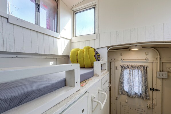 Un lit superposé avec un matelas et des oreillers, une petite fenêtre et une porte avec un rideau.