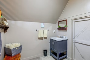 Casa de banho com lavatório branco, armários escuros, espelho, porta-toalhas e um cesto de lixo.