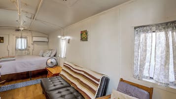 Une pièce comprenant un lit, un banc, un ventilateur et une fenêtre avec des rideaux.