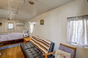 Quarto com cama, um banco, um ventilador e janela com cortinas.
