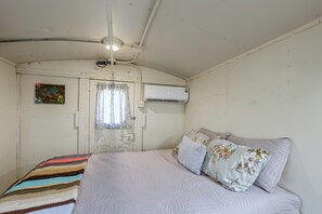 Ein Zimmer mit einem Bett, einem Vorhangfenster, einer Klimaanlage und einem an der Wand hängenden Kunstwerk.
