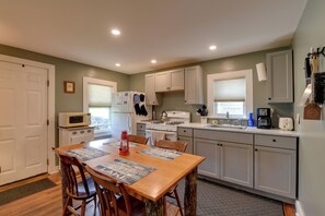 A compact kitchen with white cabinets, a microwave, a stove, and a sink. There is a dining table with chairs and a red lantern.