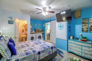 Ein Schlafzimmer mit einem Bett, einem Deckenventilator, einer Waschmaschine, einem Schminktisch und einem an der Wand befestigten Fernseher.