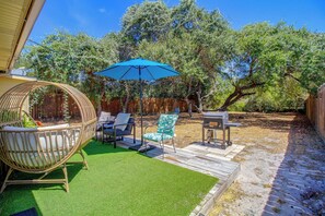 A backyard with artificial grass, a wicker chair, a blue umbrella, and a barbecue grill. - Little Minnow - Just Minutes From the Water (Aransas Pass)