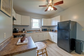 A kitchen with white cabinets, a black refrigerator, a ceiling fan, and a window.