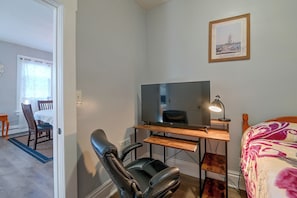 A room with a desk, a chair, a television, a bed, and a framed picture on the wall.