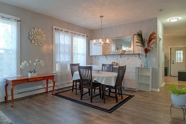 A dining area with a table set for four, wooden chairs, a chandelier, and a large mirror above the table.