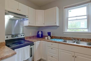 A kitchen with white cabinets, a stainless steel range hood, a blue coffee maker, and a window with a view of greenery.
