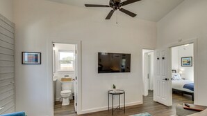 Un salon spacieux doté d’un ventilateur de plafond, d’un téléviseur fixé au mur et offrant une vue sur la salle de bain adjacente.