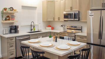 A modern kitchen with a dining table set for four, equipped with a microwave, oven, and refrigerator.