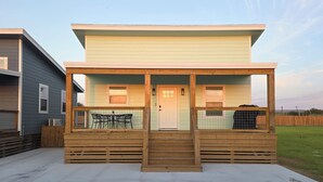 Une maison à deux étages avec un porche couvert, une porte d’entrée et un petit coin repas comprenant une table et des chaises.
