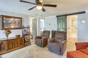 A room with a ceiling fan, a framed picture, a vase with flowers, a wooden cabinet, and a pair of armchairs. - Boat Dock! Lakefront Family Retreat in Talladega (Talladega)