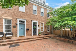 A two-story brick building with a front porch, two doors, and a small garden area with a bench and a potted plant. - Walk to Waterfront! Old Town Alexandria Escape (Alexandria)