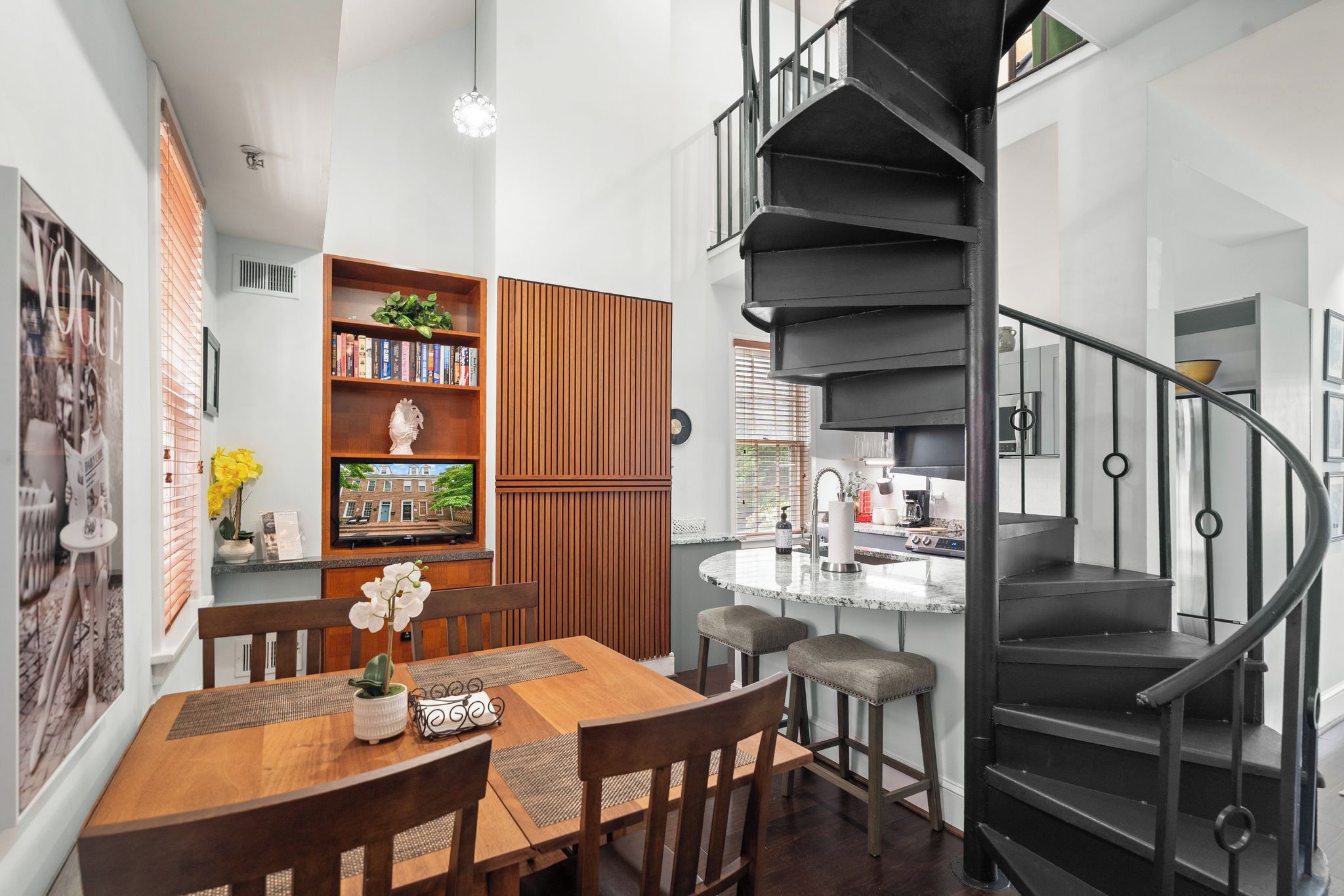 Une cuisine moderne avec un escalier en colimaçon noir, une table à manger en bois et des tabourets de bar.