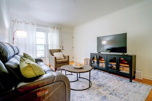 Ein Wohnzimmer mit einer Ledersofa, einem Sessel, einem Couchtisch und einem Fernseher auf einem Schrank.