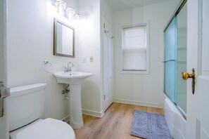 Un bagno con lavandino bianco, un water, uno specchio e lo sportello della doccia.