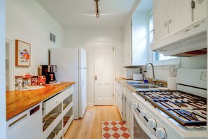 Eine kompakte Küche mit weißen Schränken, einer Holz Arbeitsplatte, einem Gasherd und einem Kühlschrank.