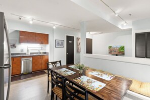 A modern kitchen with wooden cabinets, a dishwasher, and a dining area with a wooden table and chairs. - Walkable Old Town Retreat Near the Waterfront (Alexandria)