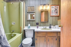 Ein Badezimmer mit einer grünen Badewanne, einer weißen Toilette, Holzschränken, einem Waschtisch mit Spiegel und einem gerahmten Bild an der Wand.