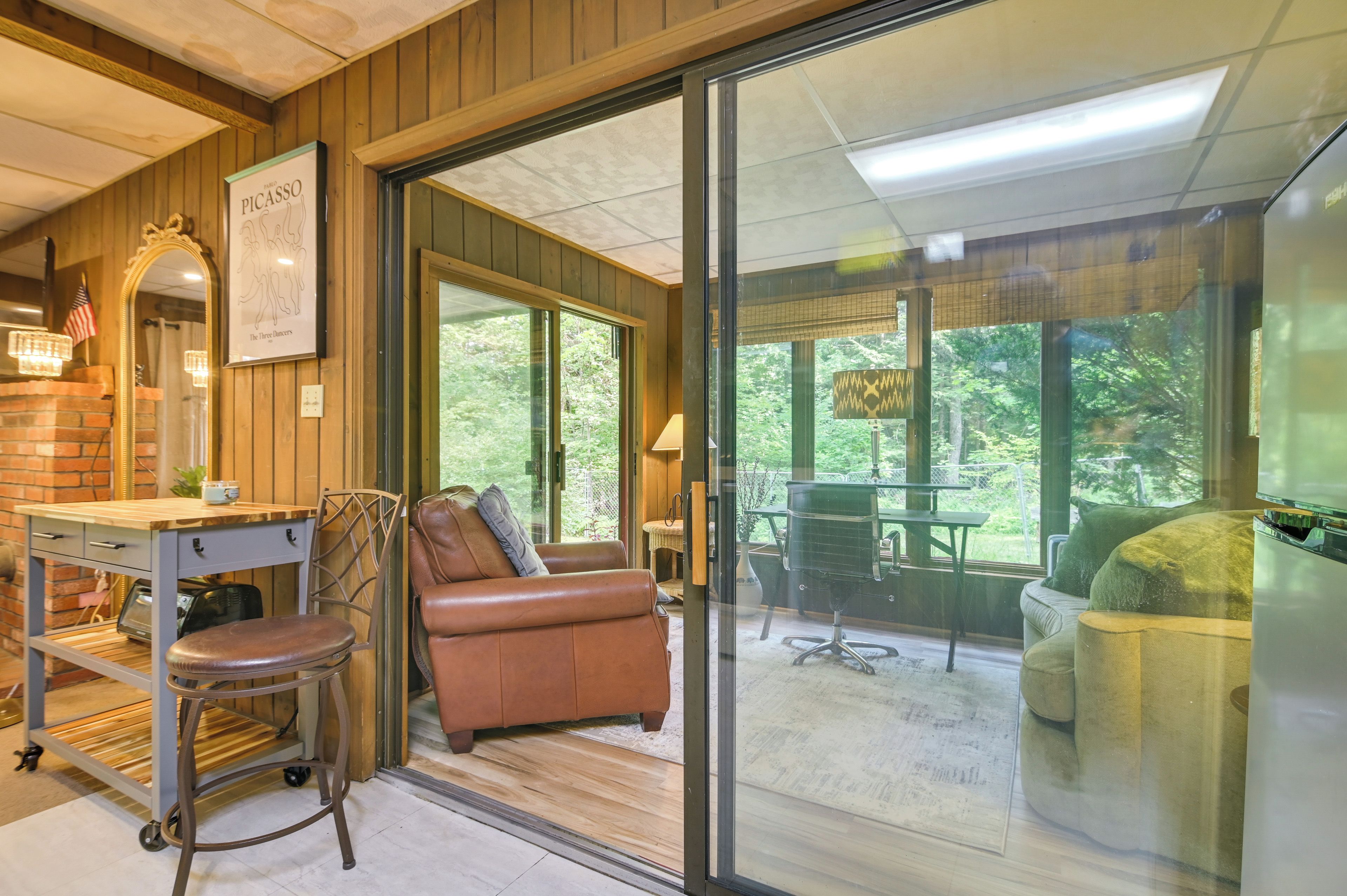 A cozy room with a wooden interior, a leather sofa, a dining table, and a large window offering a view of the outdoors.
