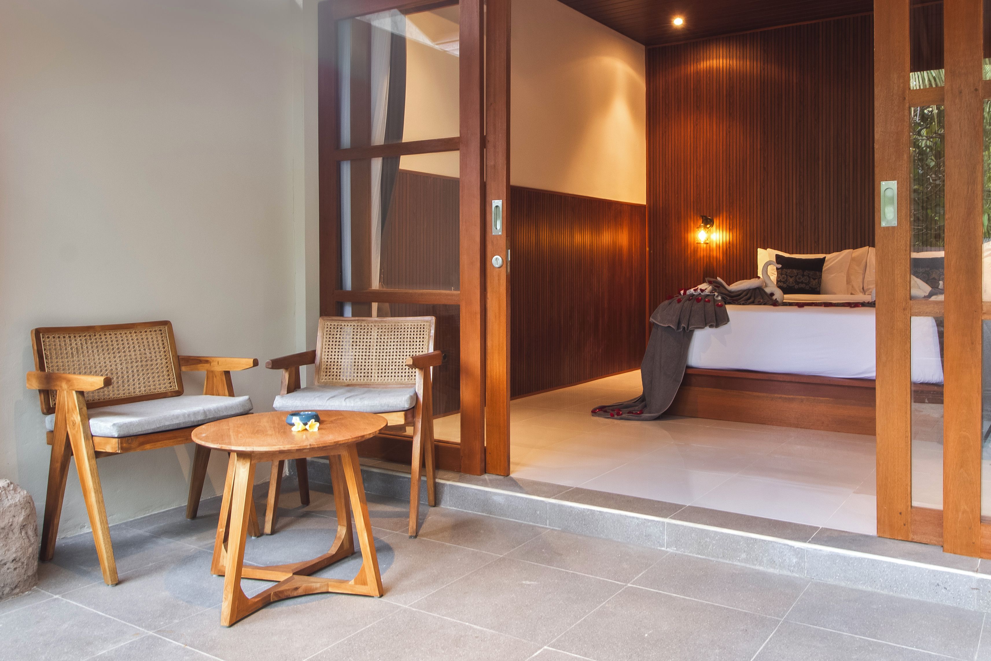 Una habitación con una cama, dos sillas, una mesita y una puerta de madera.
