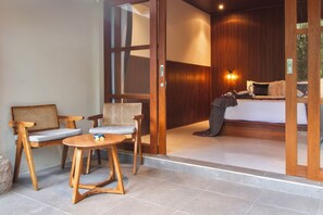 A room with a bed, two chairs, a small table, and a wooden door.