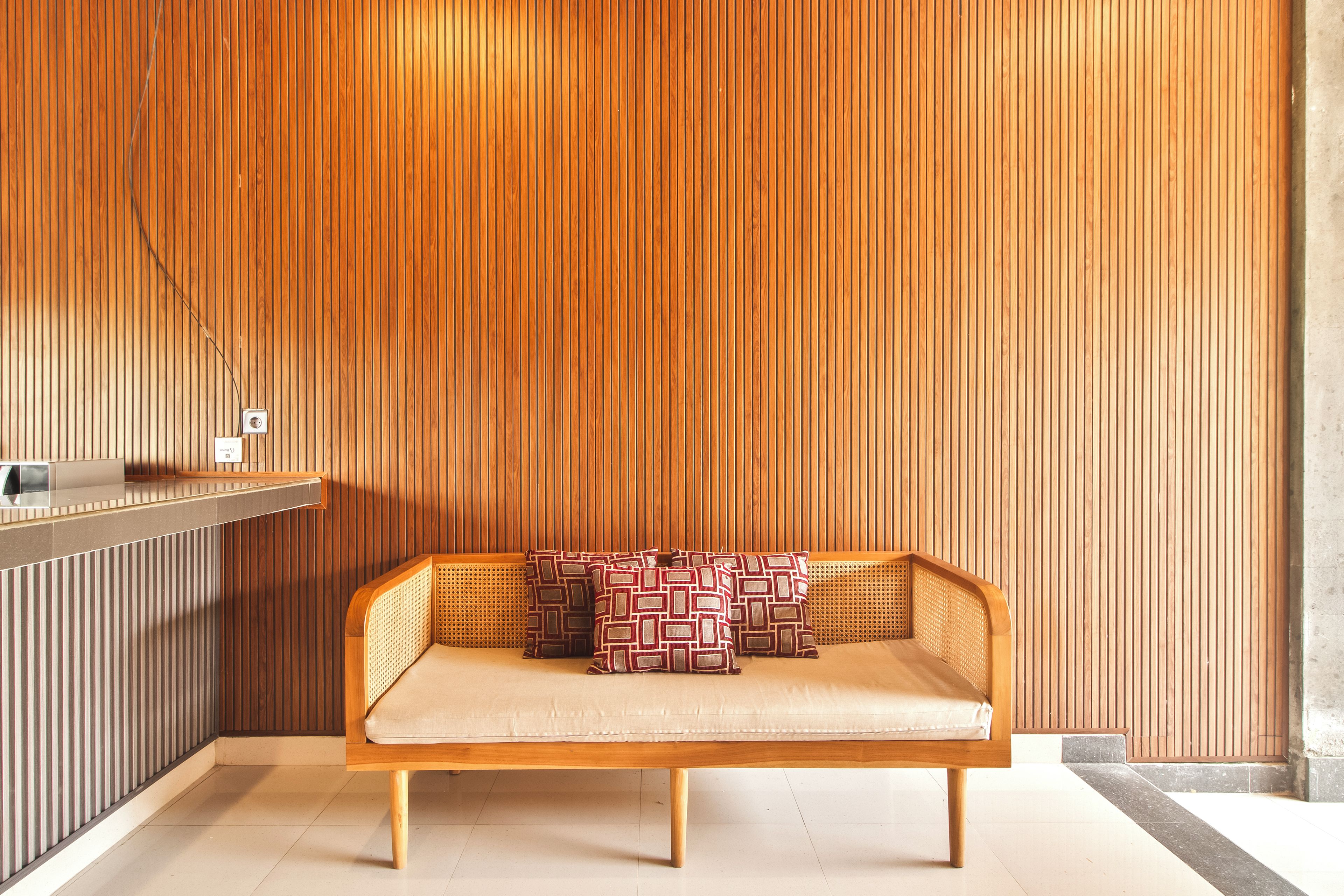 A wooden slatted wall, a wooden bench with cushions, and a small shelf with a light fixture.