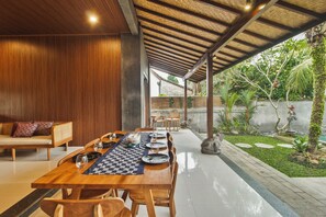 A wooden dining table set for six with chairs, a checkered table runner, and a view of a garden with a stone frog statue.