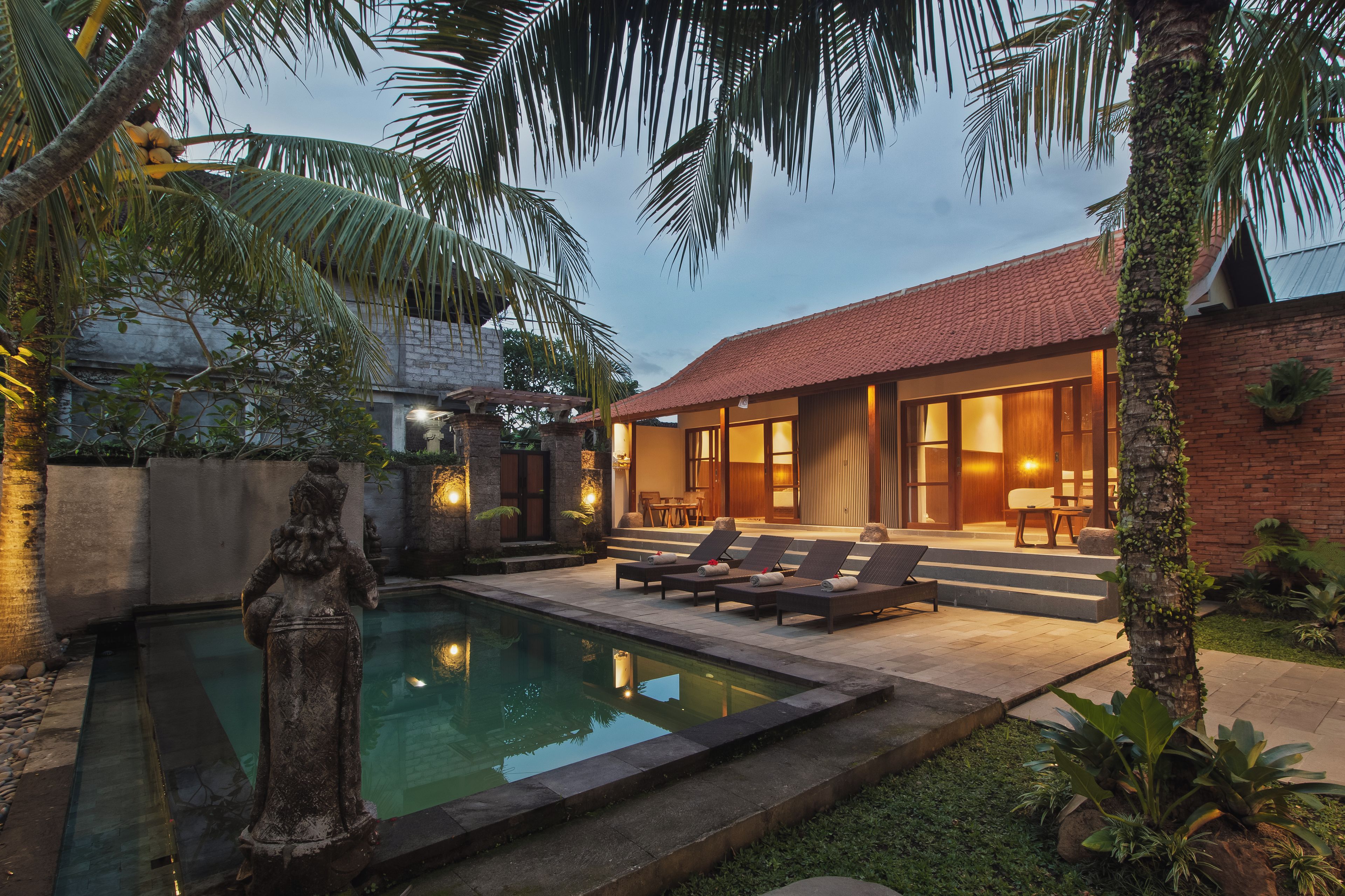A pool with lounge chairs, a stone statue, and a building with a tiled roof.