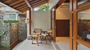 Un espacio moderno al aire libre con muros de piedra, mobiliario de madera y un ventanal que da a una habitación.