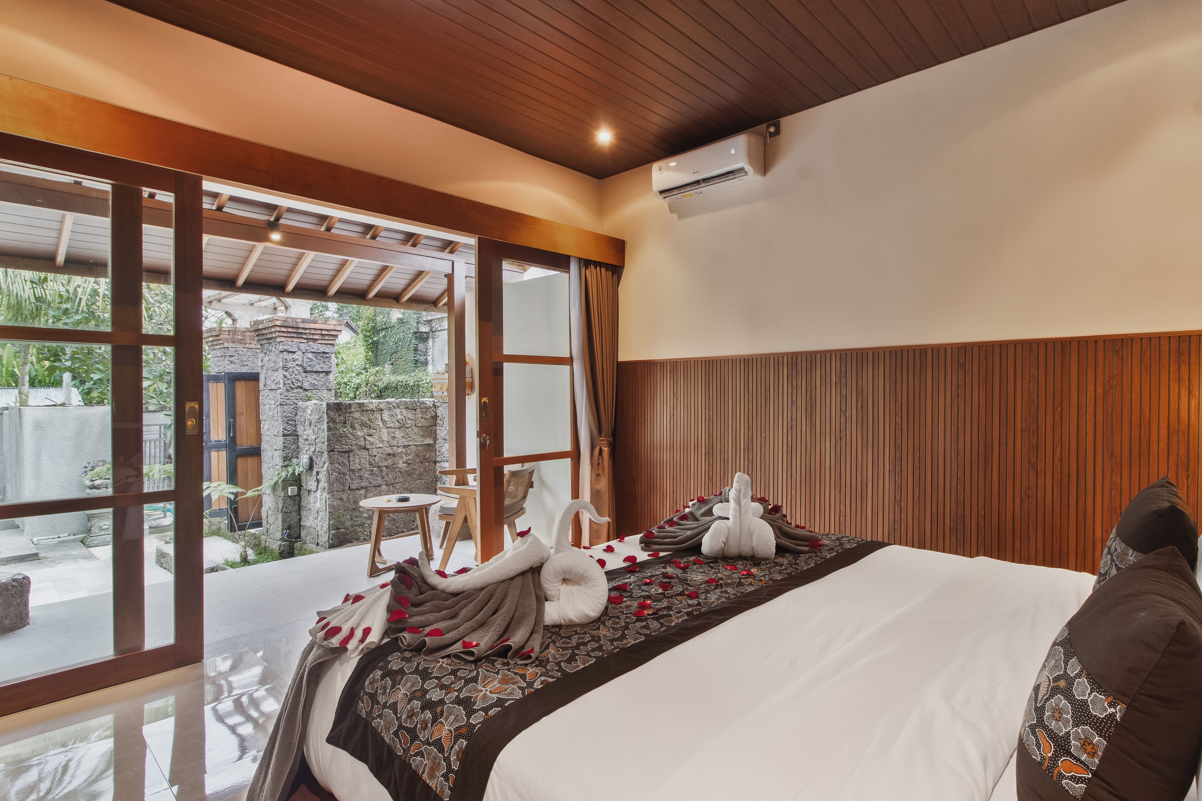 Quarto de hotel com uma cama, teto de madeira, parede de pedra e vista para o verde lá fora.
