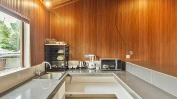 Una cocina con paneles de madera, un lavamanos, una tetera, una licuadora y un microondas.