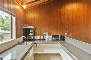 A kitchen with wooden paneling, a sink, a kettle, a blender, and a microwave.