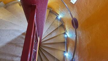 A spiral staircase with a red handrail and lights, leading to a higher floor.