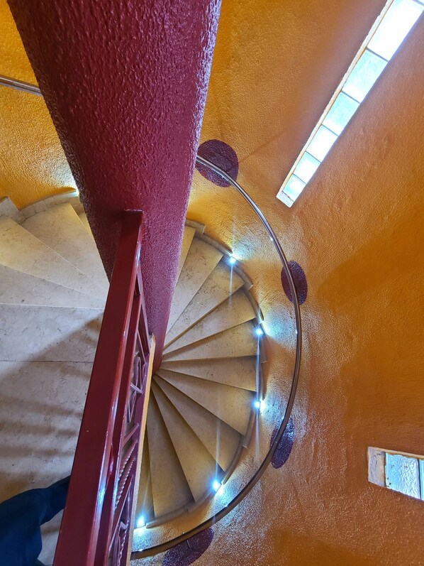 A spiral staircase with a red handrail and lights, leading to a higher floor. - Quiet Pols Residence (Lagos)