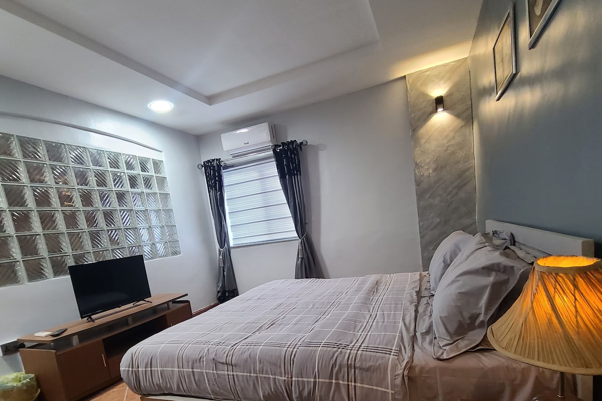 Un dormitorio con cama, televisión, lámpara y ventana con cortinas.