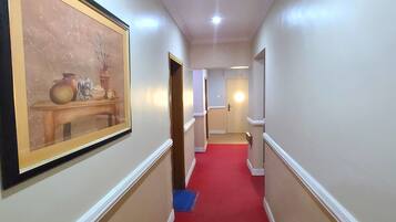 A hallway with a red carpet, white walls, and a framed artwork on the left.