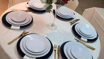 A round table set for a meal with white plates, blue rimmed plates, gold cutlery, and a vase with flowers.