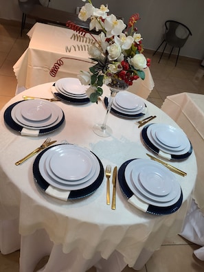 A round table set for a meal with white plates, blue rimmed plates, gold cutlery, and a vase with flowers. - Quiet Pols Residence  (Lagos)