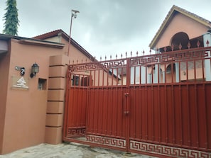 A gated entrance with a security sign, a lamp post, and a building with a numbered sign. - Quiet Pols Residence  (Lagos)