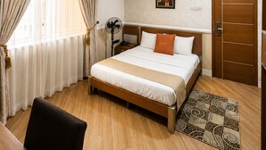 A hotel room with a bed, bedside table, fan, air conditioning unit, and a door. - Quiet Pols Residence  (Lagos)