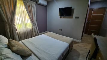 Une chambre d’hôtel équipée d’un lit, d’un bureau, d’un climatiseur, d’une télévision et d’une porte.