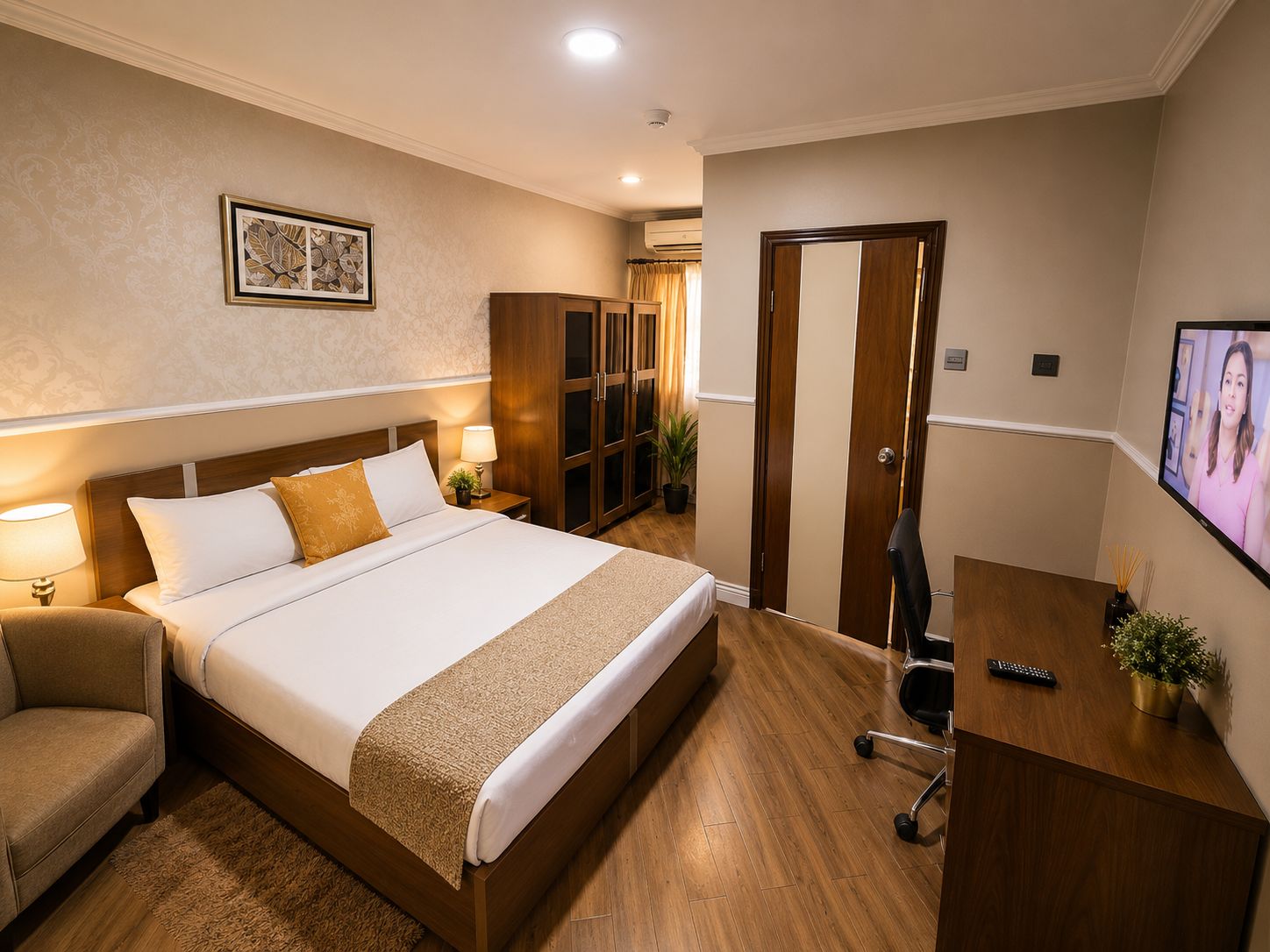 A hotel room with a bed, bedside table, chair, desk, TV, wardrobe, and a potted plant.