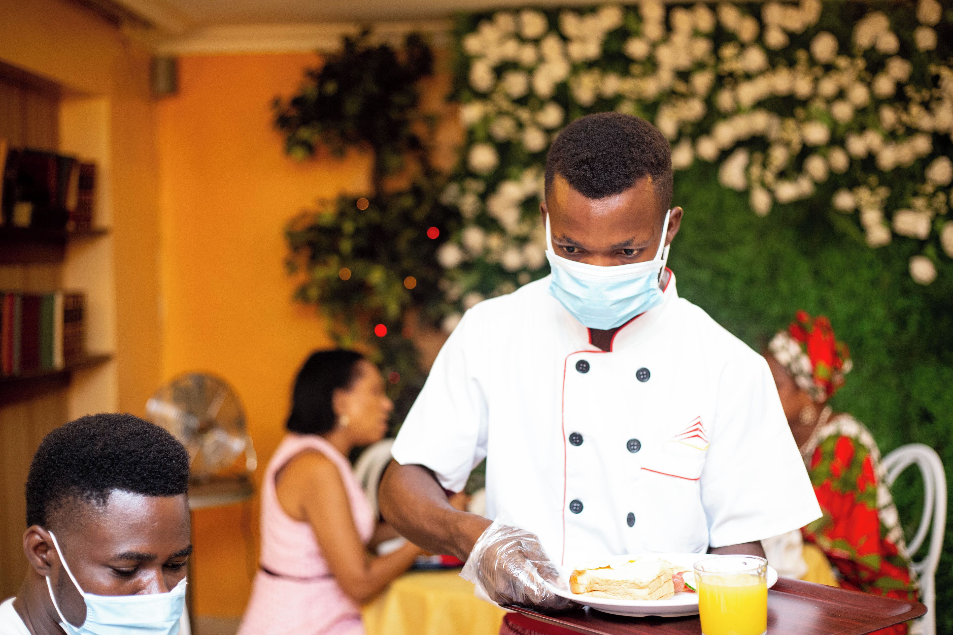 A person in a white chef's uniform serving food to guests at a table.