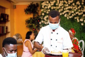 A person in a white chef's uniform serving food to guests at a table. - Quiet Pols Residence (Lagos)