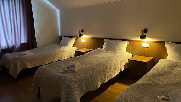A hotel room with three single beds, each with a wooden headboard and bedside tables. - Mirano Guest House Hostel  (Karakol town)